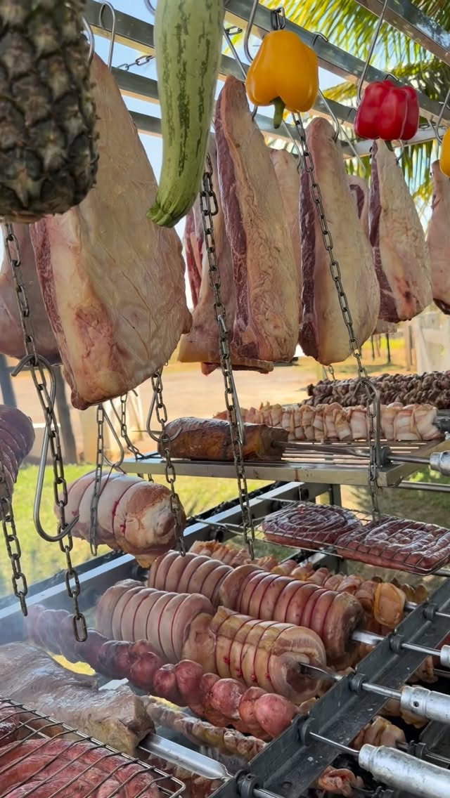 Peças de carne penduradas em ganchos ao redor do fogo de chão.